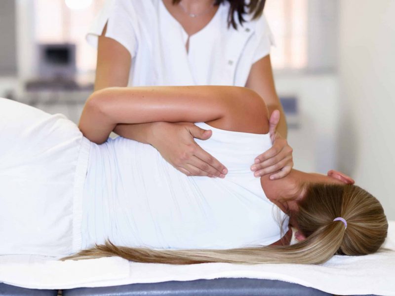 Professional female physiotherapist giving shoulder massage to blonde woman in hospital. Medical check at the shoulder in a physiotherapy center.